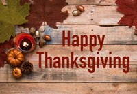 A wooden table setup with a candle, gourds, and leaves with the words HappyThanksgiving.