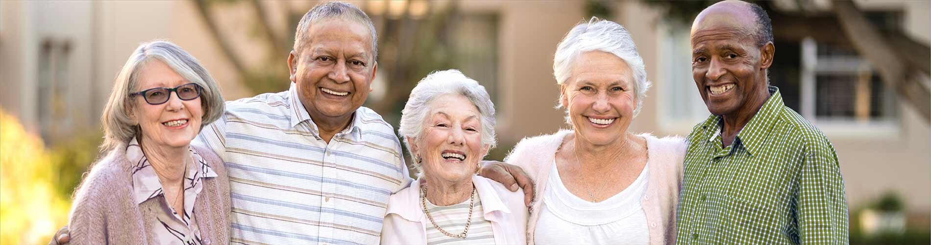 A group of older men and women smile for a photograph outside of their housing units.