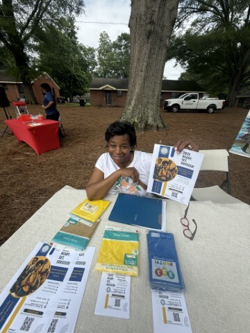 Woman seated at a table holding up a promotional brochure. 