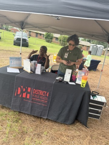 Two women at a tent with a table with the text, DPH District 4 Public Health.