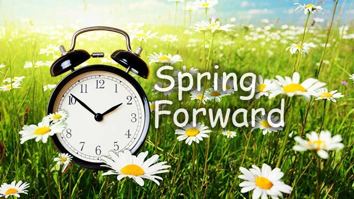 An alarm clock in a field of flowers with the text, Spring Forward. 